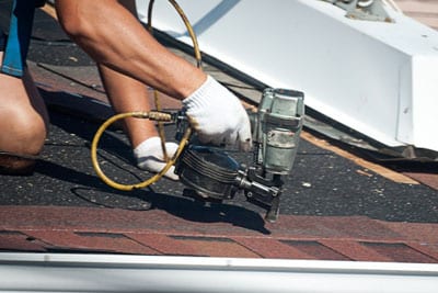 A roofer using gloves and a tool to prep the laying down of shingles on a house.